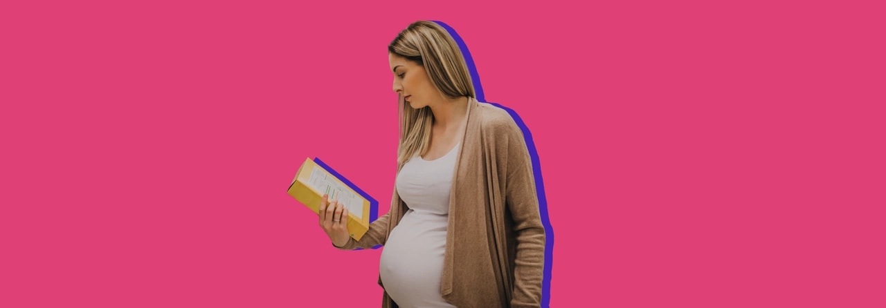 Pregnant woman in a cardigan reading the information on the back of a product box