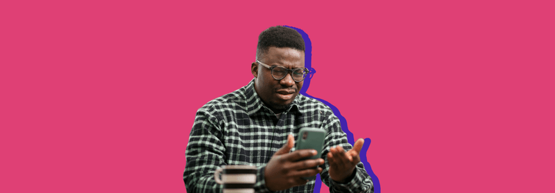 A young Black man in a checked shirt looking down at his smartphone, set against a bright pink background.