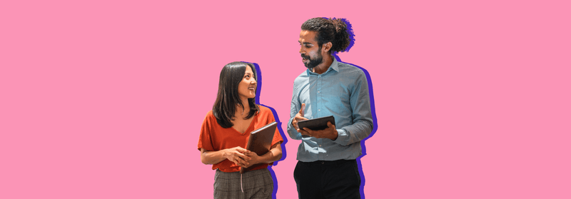Two colleagues talking, one holding a notebook and the other a tablet, set against a pink background.