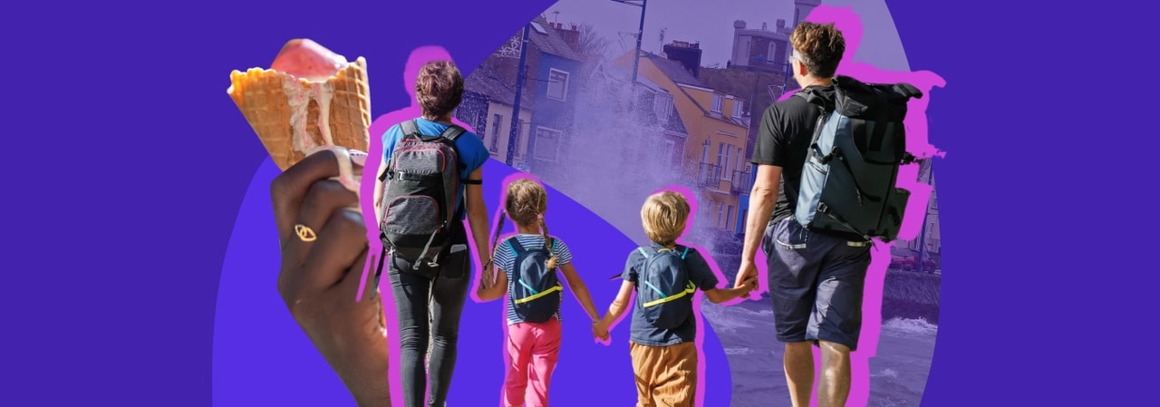 Parents and two children walking hand in hand down a seaside street, with a hand holding an ice cream in the foreground