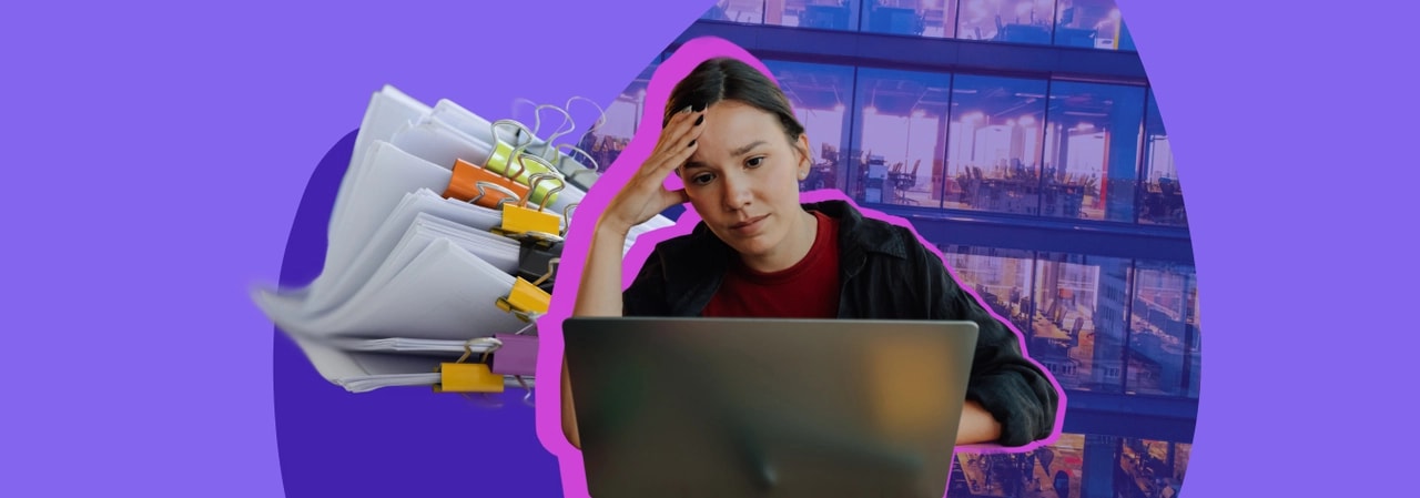 Stressed woman holding her forehead at a laptop, with a large pile of paperwork beside her and an office behind