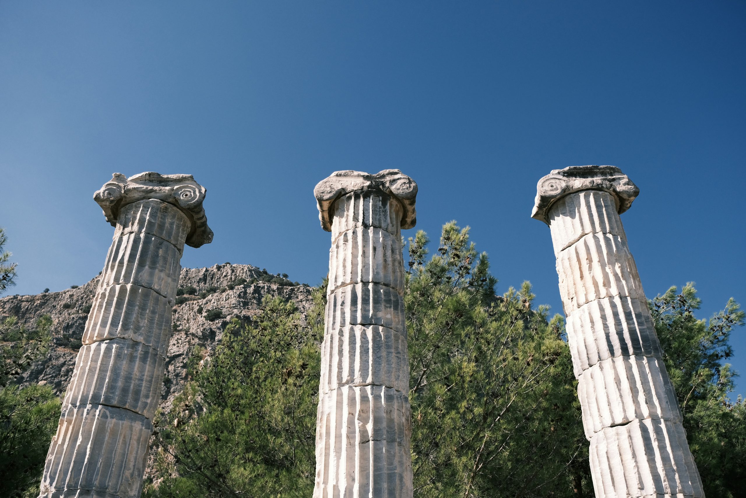 Three ancient stone pillars standing against a clear blue sky and mountainous landscape, symbolizing the three foundational pillars that support a strong customer-centric business strategy.