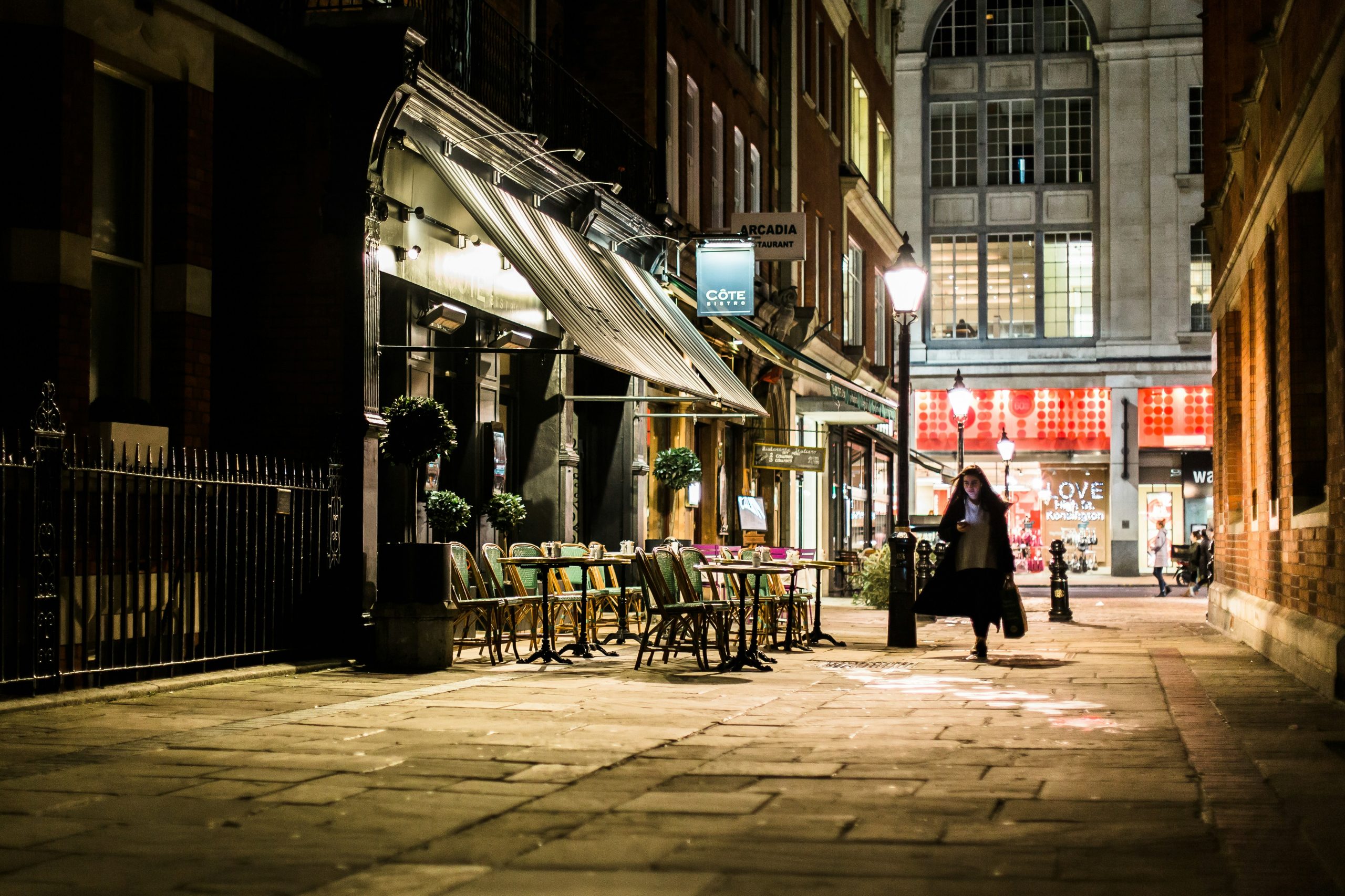 A dimly lit UK city street with quiet restaurants and empty outdoor seating at night, representing low UK consumer confidence driven by economic uncertainty, rising living costs, and reduced consumer spending.
