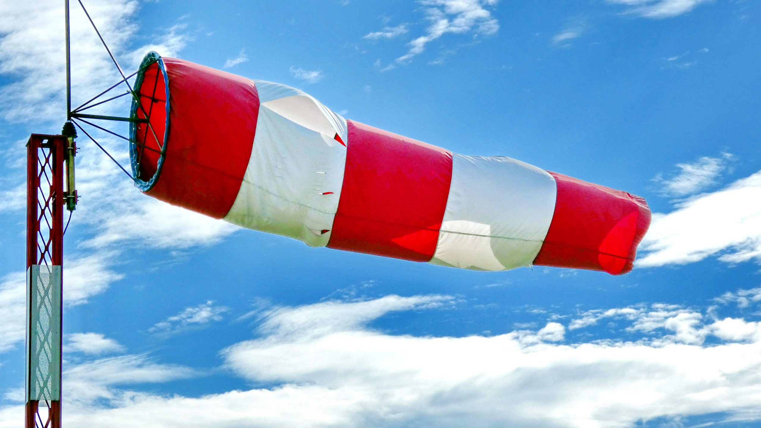 A large red-and-white striped windsock stretched out in strong wind against a bright blue sky with scattered white clouds, symbolizing uncertainty and changing market conditions in a low-confidence demand environment.