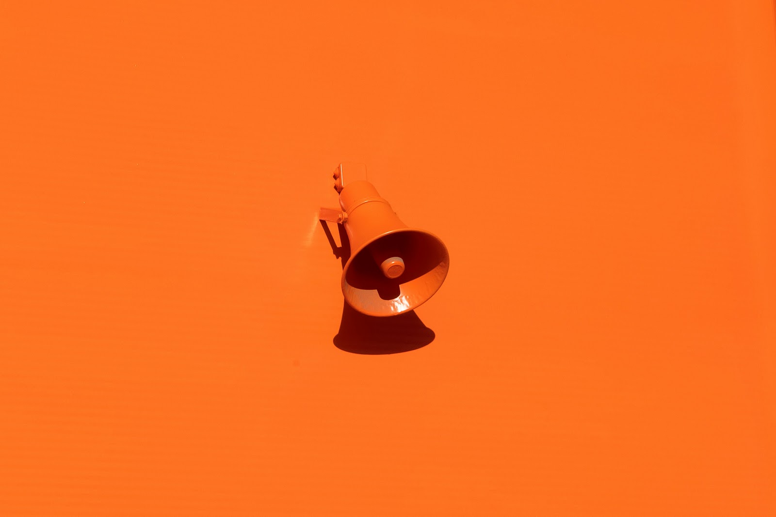 A bright orange megaphone placed against a matching orange background, symbolising the psychological factors that influence consumer behaviour, such as perception, motivation, attention, and persuasive messaging.